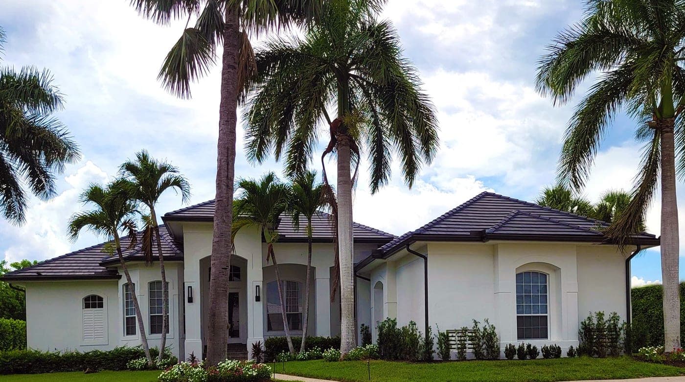 A white single-story home with a tile roof, tidy lawn and tall palms under a blue sky
